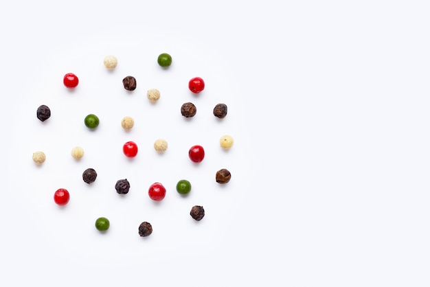 Red, green, white and black peppercorns on white
