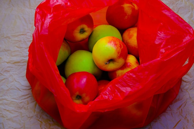 빨간 녹색 노란 사과 는 플라스틱 빨간 가방 에 있는 공예 종이 에 놓여 있다