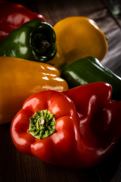 Red, green and yellow bell peppers, lit on a wooden table.