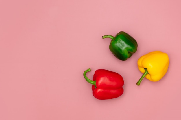 Red, green and yellow peppers on pink background