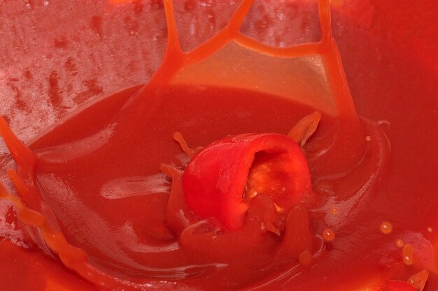 Red grocery background of tomato juice with sweet pepper splash close-up