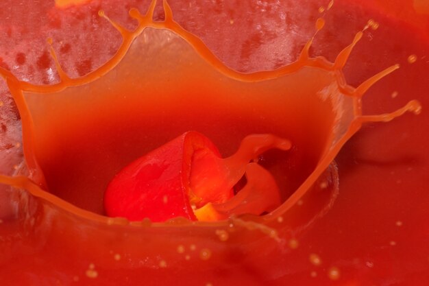 Red grocery background of tomato juice with sweet pepper splash close-up