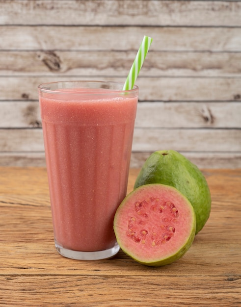 Red guava juice in a glass with ice and fruits over wooden table.