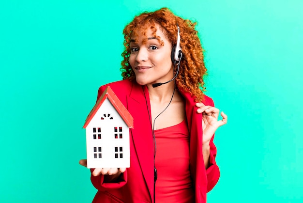 Foto agente dello stato reale della donna graziosa dei capelli rossi con un modello di casa e un auricolare