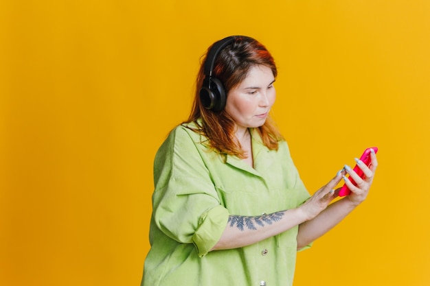 Рыжая женщина слушает музыку на телефоне через наушники