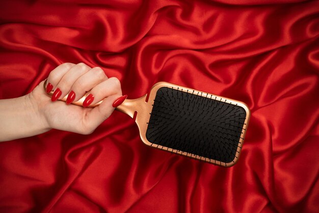 A red hairbrush in woman hand on a red silk background