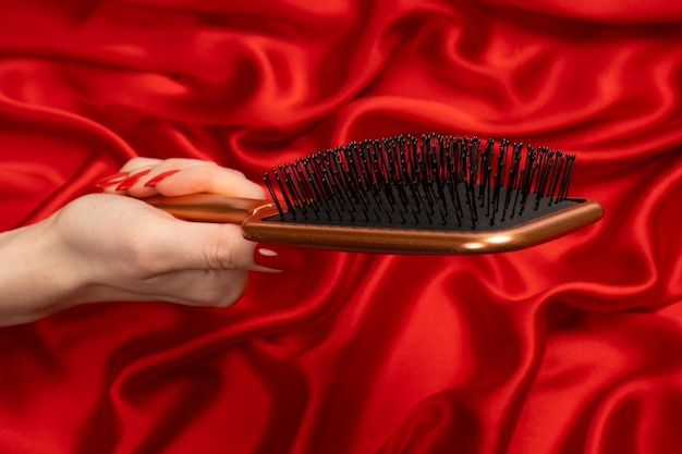 A red hairbrush in woman hand with red nails ion a red background Beauty tools Hair tools