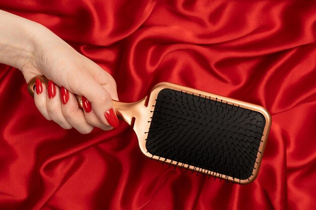 A red hairbrush in woman hand with red nails ion a red background