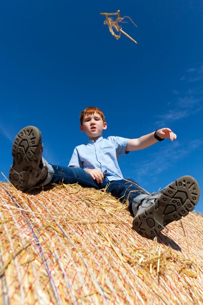 Red-haired boy sitting on a golden straw stack in a field