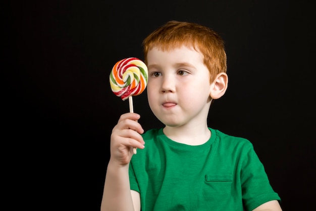 A red-haired boy with a sweet multi-colored candy on a stick