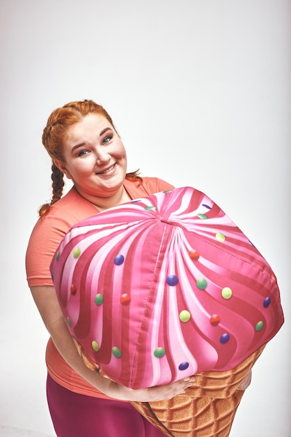Red haired chubby woman is holding a huge ice cream closeup