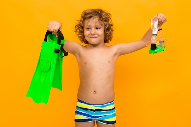 Red-haired curly boy holds swimming flippers on a yellow background