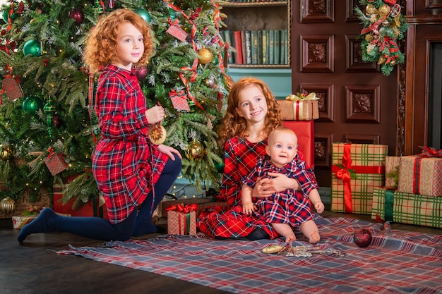 Red-haired curly children decorate the Christmas tree in a beautiful cozy interior.