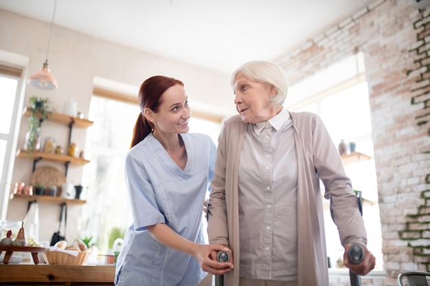 Red-haired female caregiver supporting woman with crutches