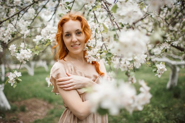 Red-haired girl in a beige dress in the garden