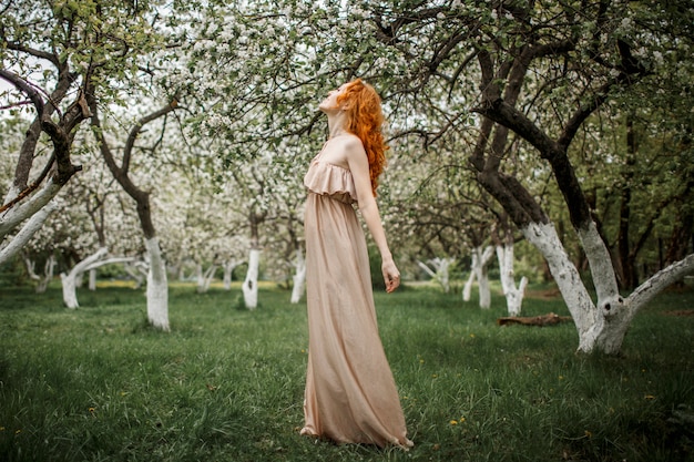 Red-haired girl in a beige dress in the garden