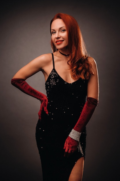 Red-haired girl in a black dress and elegant gloves on a black background