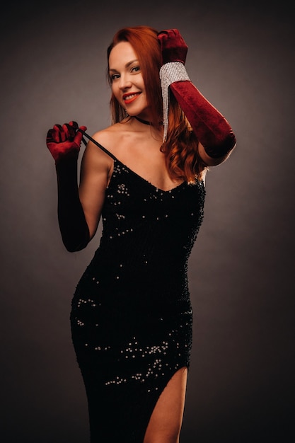 Red-haired girl in a black dress and elegant gloves on a black background