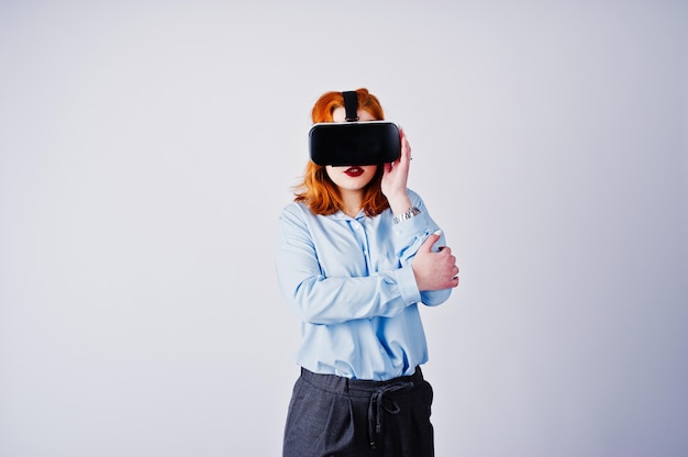 Red haired girl in blue blouse with vr glasses  isolated on white.