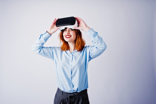 Red haired girl in blue blouse with vr glasses  isolated on white.