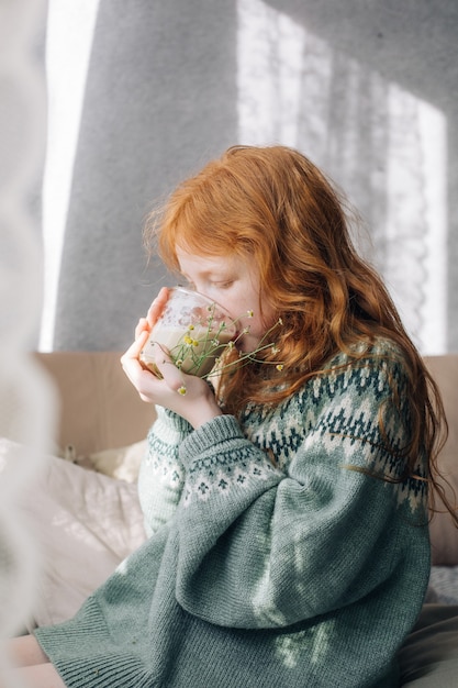 赤毛の少女はガラスのグラスから朝のコーヒーを飲みます。