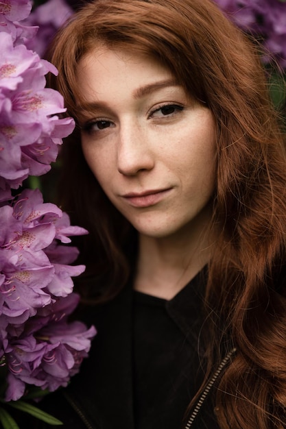 A red-haired girl of European appearance with freckles stands near the gray. bouquets of beautiful lilacs behind a girl. spring flowers. International Women's Day