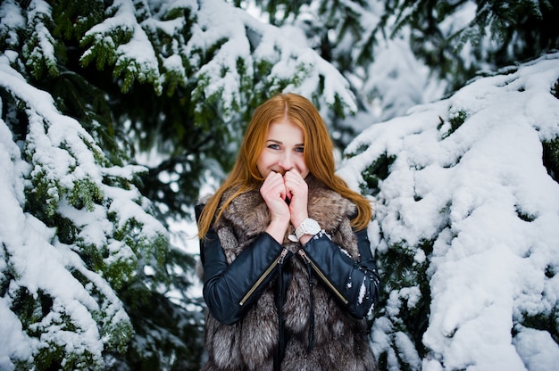 Red haired girl in fur coat walking at winter snowy park.