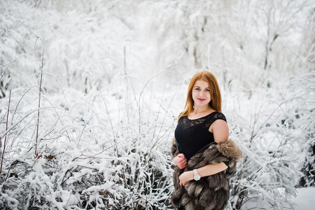 Red haired girl in fur coat walking at winter snowy park