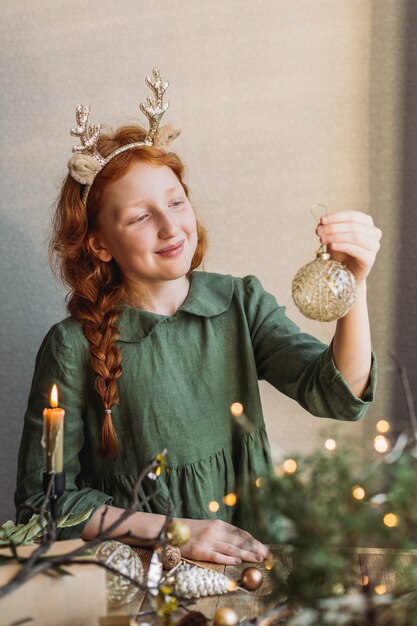 A red-haired girl in a green linen dress looks at Christmas decorations.