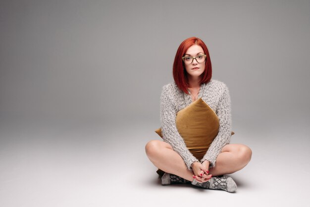 Red haired girl in grey sweater and warm socks sitting on floor