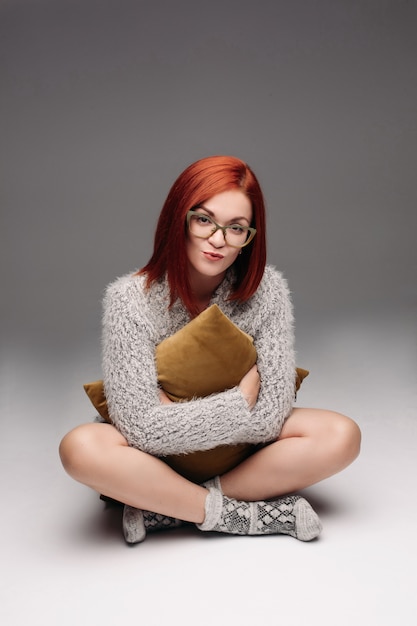 Red haired girl in grey sweater and warm socks sitting on floor