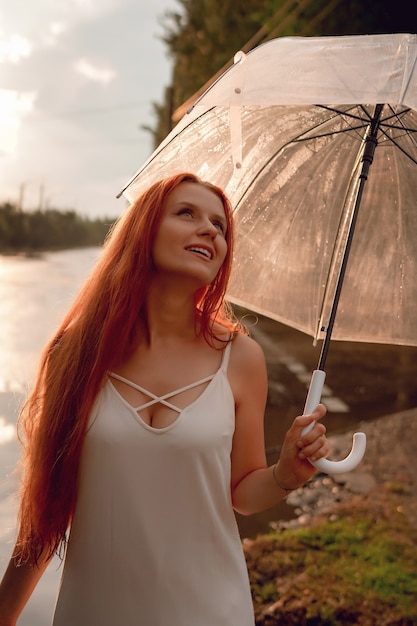 写真 雨の後の傘と白いドレスを着た赤い髪の少女