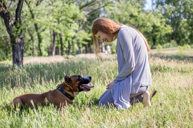 赤い髪の少女は公園で犬と遊んでいます。