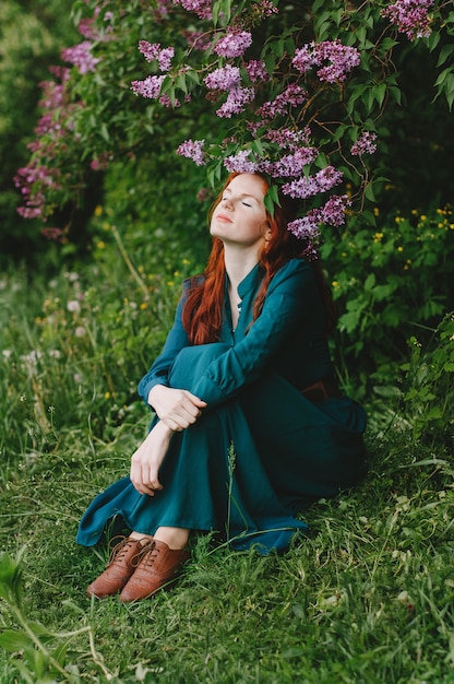 The red-haired girl is standing near the lilac bush