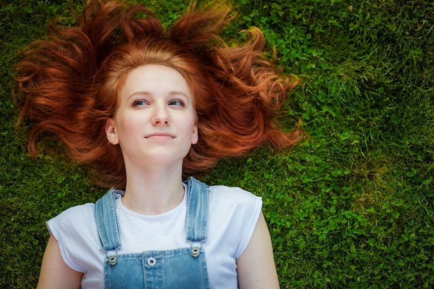 Red-haired girl lying on the green grass copy space