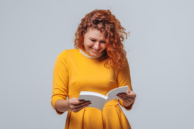 Red-haired girl reading a white book on a light gray background.