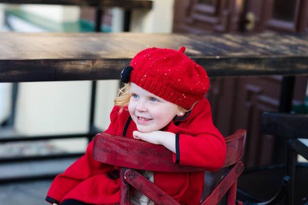 Red-haired girl in a red coat and a beret sits on a chair