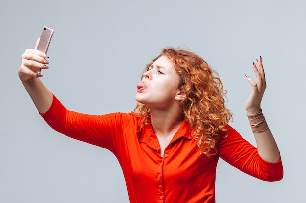 Red-haired girl takes a selfie on the phone on a light gray background