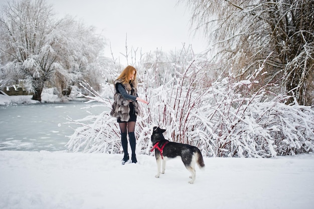 Red haired girl walking at park with husky dog on winter day.