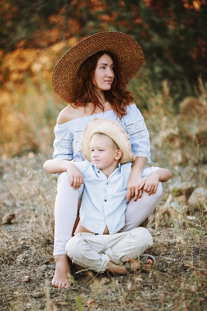 Red-haired girl with a child against the backdrop of a sunset. Cute mother with a blond baby