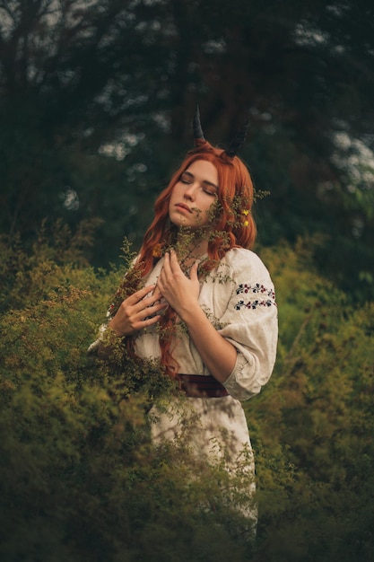 Foto ragazza dai capelli rossi con le corna in un vyshyvanka bianco nel parco