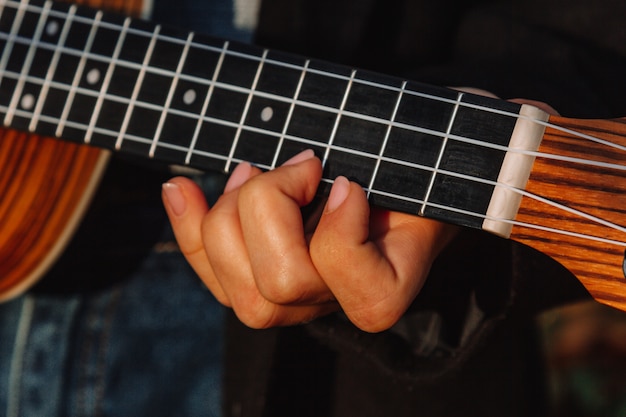 Red-haired girl with long hair plays on the ukulele in the park. School, music education concept, student learns to play the string instrument. Hands of a musician, classical, melody, creativity.