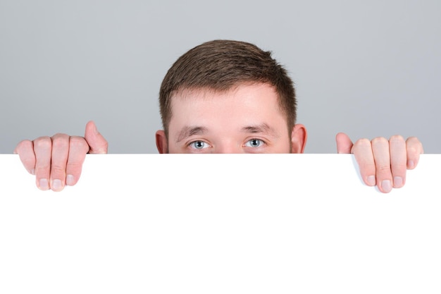 A red-haired man looks out from behind a white blank board