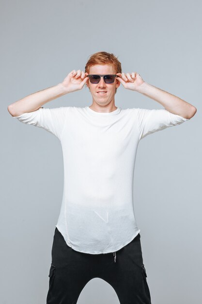 red haired man in sunglasses and a white t-shirt posing on a light background