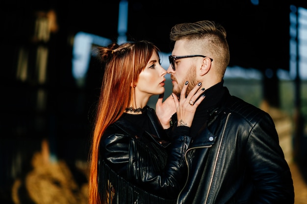A red-haired, thin girl in black clothes touches her boyfriend's beard in an abandoned building at sunset