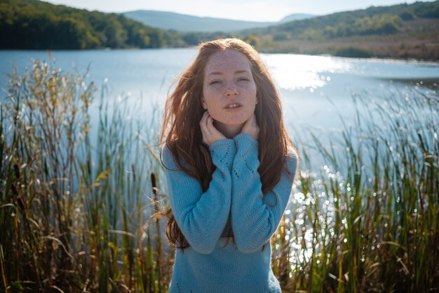 Photo red-haired woman at the beach by the lake in fall clothing.