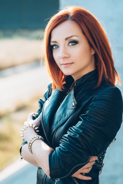 Red-haired woman in a black leather jacket on a concrete wall