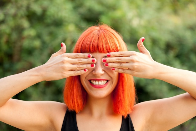 Red haired woman covering her eyes in a park