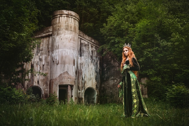 城の近くの緑の中世のドレスを着た赤毛の女性
