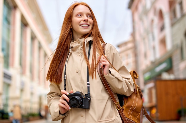 Red-haired woman tourist with retro camera in historical old
city. free casual style